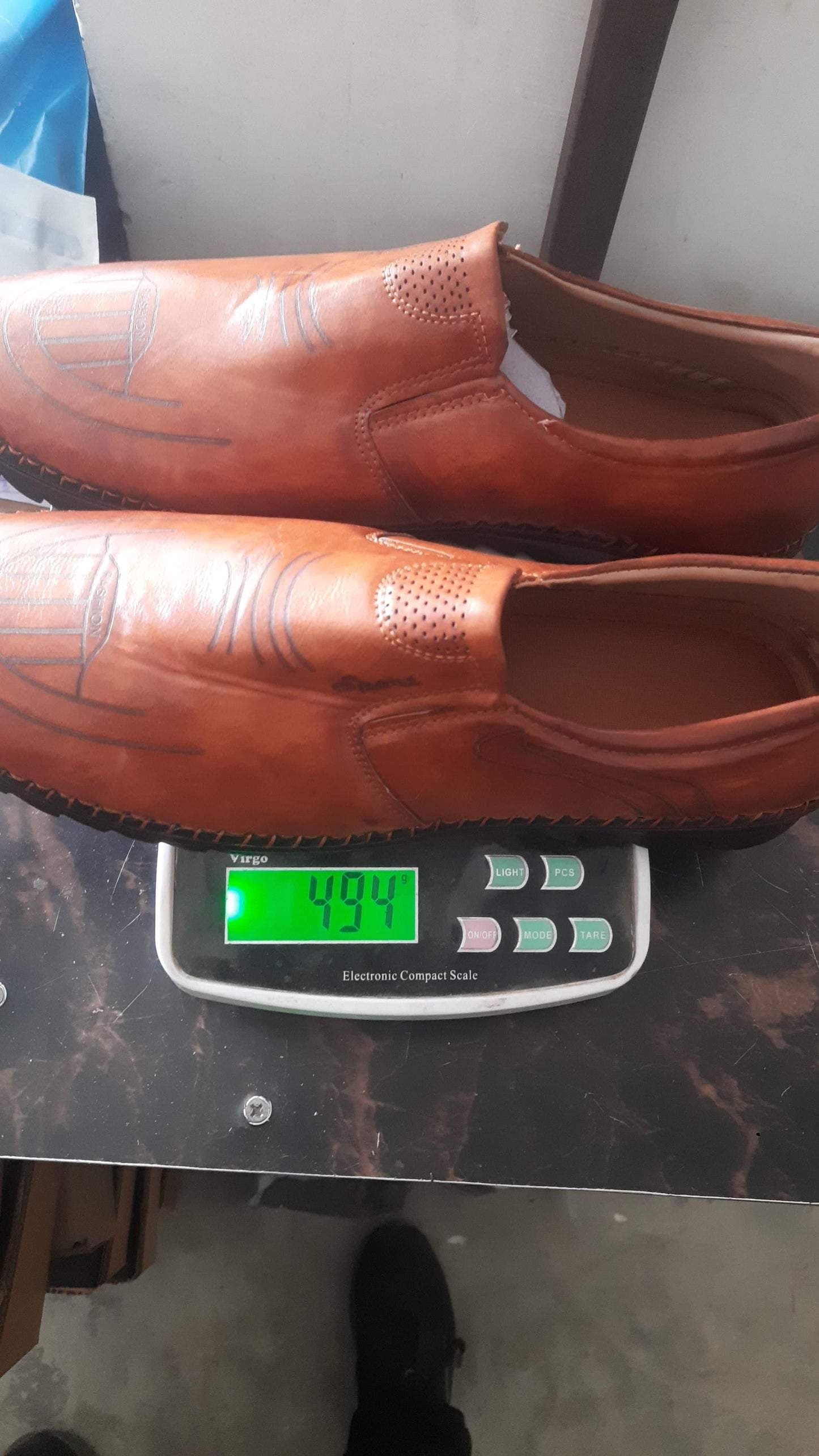 Mens brown leather shoes on a digital scale showing weight of 494 grams, perfect for stylish comfort.